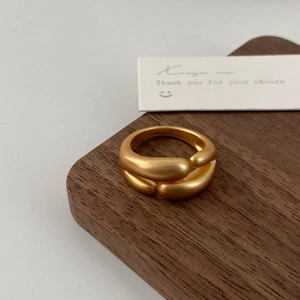 Makro-Detail des mattgoldenen Crossover-Rings mit dicken runden Enden auf Holzständer
