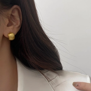 Macro side view of golden chunky brushed metal earrings on model with satin fabric