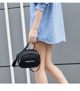 Detail of a black mini crossbody bag with white lettering and dual zipper compartments