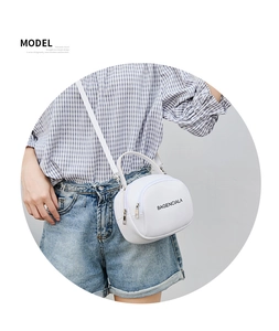 Close-up of white round crossbody bag with black lettering and silver metal zippers