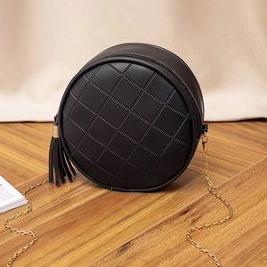 Black quilted circular crossbody bag with tassel and gold chain on wooden floor