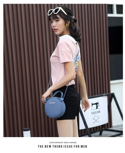Close-up of a light blue round leather crossbody bag featuring lychee grain texture and logo