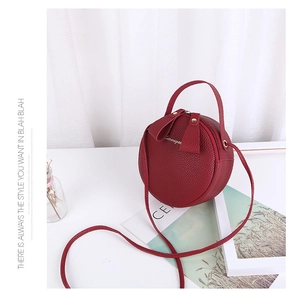 Detail shot of a round burgundy crossbody bag with lychee texture and bow zippers