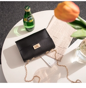 Detail view of a black chain bag with gold hardware on a table with a tulip