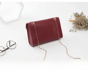 Détail d'un sac à bandoulière bordeaux avec chaîne dorée dans un décor minimaliste