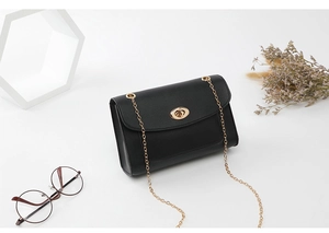 Détail du sac bandoulière en cuir noir avec chaîne dorée et fermoir ovale élégant