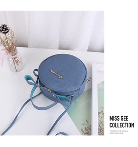 Detail of blue pebble leather round bag with bow accent and gold logo lettering
