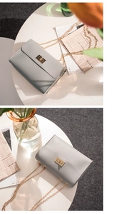 Detail of grey pebbled leather crossbody bag with golden chain and twist lock on a table