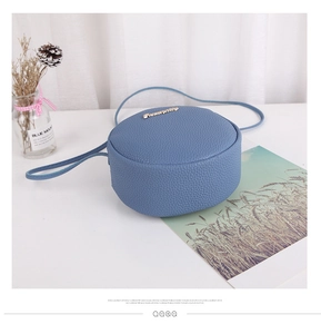 Macro shot of blue circular crossbody bag with litchi grain texture and gold logo