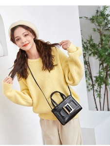 Detail of black crocodile pattern crossbody bag with gold square buckle shown on a model