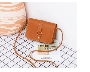 Detail of tan square crossbody bag with white stitching and gold ring buckle closure