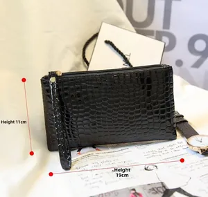 Vue détaillée d'une pochette noire à motif crocodile avec zip doré et dragonne