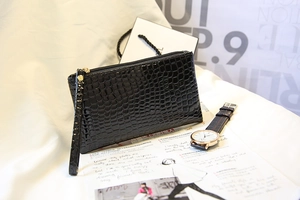 Détail d'une pochette noire à texture crocodile avec zip doré et dragonne assortie