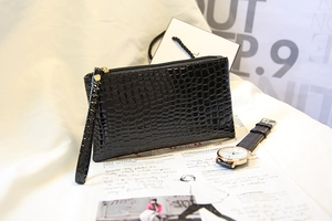 Détail de la pochette noire à texture crocodile avec zip doré et dragonne amovible