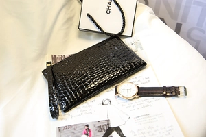 Détail d'une pochette noire à texture crocodile avec zip doré et dragonne élégante
