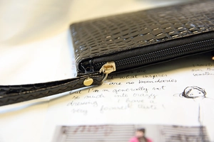 Gros plan d'une pochette noire à motif crocodile avec fermeture éclair dorée et dragonne
