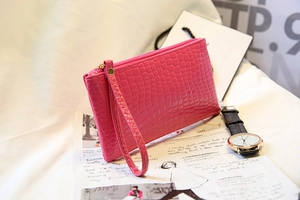Vue détaillée d'une pochette rose rouge à motif crocodile avec dragonne et fermeture