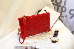 Détail d'une pochette en cuir verni rouge à motif crocodile avec fermeture éclair dorée