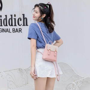 Petit sac à dos bicolore rose et beige avec rabat et boucles décoratives sur un banc blanc