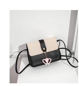 Detail shot of a small black and cream crossbody bag with a pink heart pendant charm