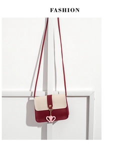 Detail of burgundy and cream crossbody bag with gold buckle and pink heart charm