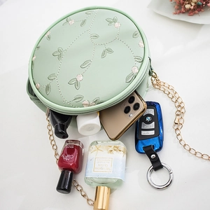 Sac bandoulière rond vert menthe avec broderie florale et chaîne dorée sur fond blanc