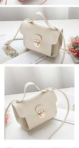 Close-up of a cream-colored square crossbody bag featuring a gold round clasp and handle