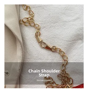 Close-up of a glossy gold chain strap with metallic links on a textured fabric surface