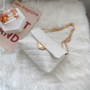Elegant white quilted chain handbag with gold diamond clasp on a soft white plush rug