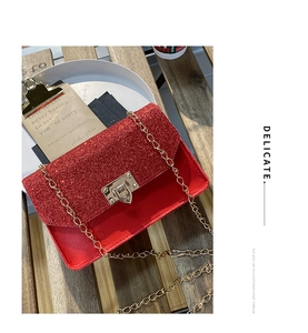 Detail of red sequin crossbody bag with gold buckle and chain on a wooden table