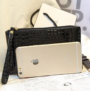 Pochette noire brillante à motif crocodile avec dragonne à côté d'un smartphone