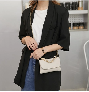 Sac bandoulière ivoire avec chaîne en résine sur un mannequin en blazer noir