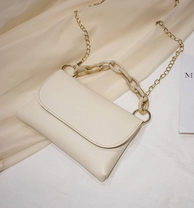 Détail d'un sac bandoulière beige crème avec d'élégantes chaînes en métal et acrylique