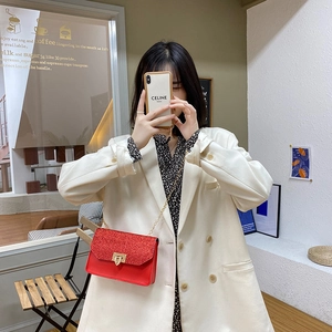 Women's red sequined chain crossbody bag with gold lock shown in a stylish cafe setting
