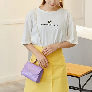 Light purple crocodile pattern handbag with gold chain strap worn over a yellow skirt