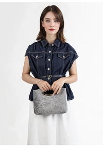 Close-up of grey textured handbag with gold circular metal handle held by a model