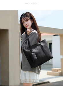 Detail of a large black woven tote bag with matching charm on a grey blazer model