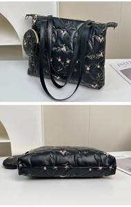 Detail of black quilted tote bag featuring pink floral embroidery and mini round pouch