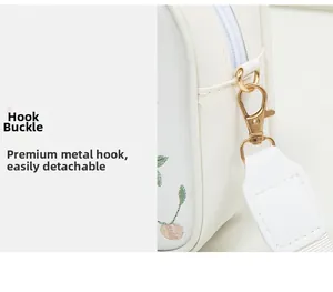 Close-up of golden metal hooks and detachable shoulder strap on a white floral handbag