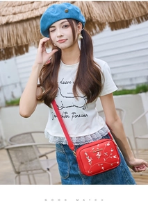 Close-up of red crossbody bag with floral embroidery and adjustable wide shoulder strap