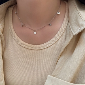 Nahaufnahme einer silbernen Kette mit fünf runden Anhängern auf beigem Strickpullover
