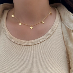 Nahaufnahme einer goldenen Halskette mit fünf runden Anhängern auf einem Strickpullover