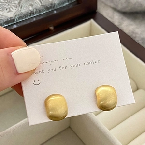 Detail showing matte gold oval stud earrings with brushed texture on white display card