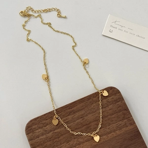 Detailaufnahme einer zarten Goldkette mit fünf kleinen massiven Herzanhängern und Karabinerverschluss
