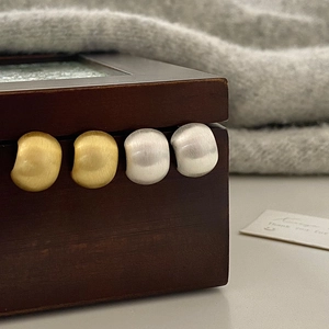 Detailed view of brushed metal stud earrings in gold and silver on wooden box