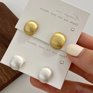 Macro shot of matte brushed flat round earrings in gold and silver finish on display card