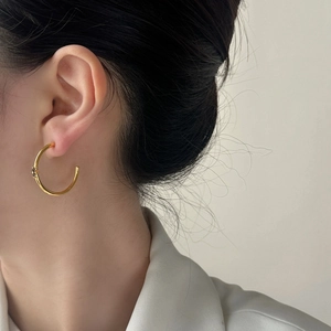 Elegant gold C-shaped hoop earrings with black zircon flower detail worn by a model