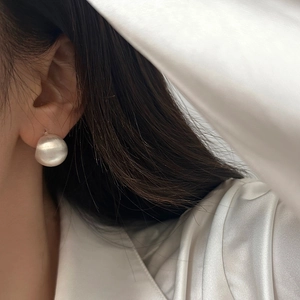 Gros plan d'une boucle d'oreille ronde en métal satiné argenté portée par un mannequin