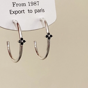 Macro view of C-shaped silver earrings with black clover floral design on a display card