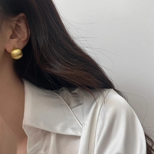 Gros plan sur des boucles d'oreilles boules dorées brossées portées par un mannequin